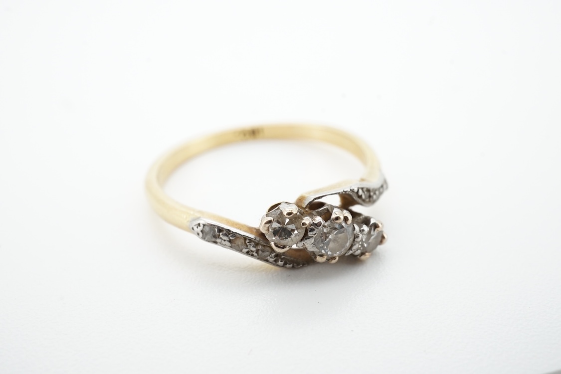 A three-stone diamond ring, early 20th century, centring on a diagonal line of three circular-cut diamonds totalling approximately 0.24 carats, to asymmetrical shoulders set with smaller rose-cut diamonds, mounted in gol